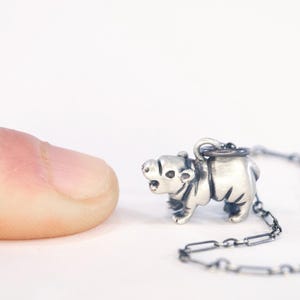May include: A small, silver-colored pendant necklace featuring a detailed polar bear charm. The bear is standing, with visible features. The necklace chain is also silver. The image is set against a white background.