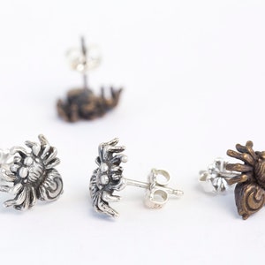 May include: Three pairs of spider earrings, one pair is silver, one pair is bronze, and one pair is gold.
