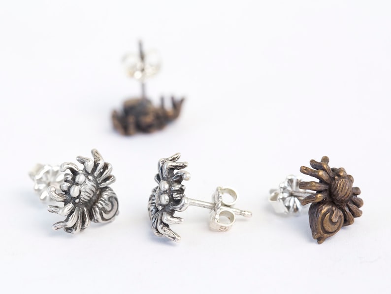 May include: Three pairs of spider earrings, one pair is silver, one pair is bronze, and one pair is gold.