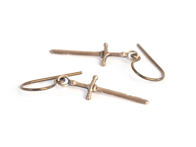 May include: A pair of gold-toned sword earrings with a simple hook design.