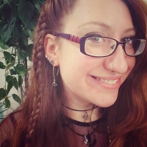 May include: A woman with long brown hair styled in a braid, wearing glasses, a black choker necklace, and a black lace top.
