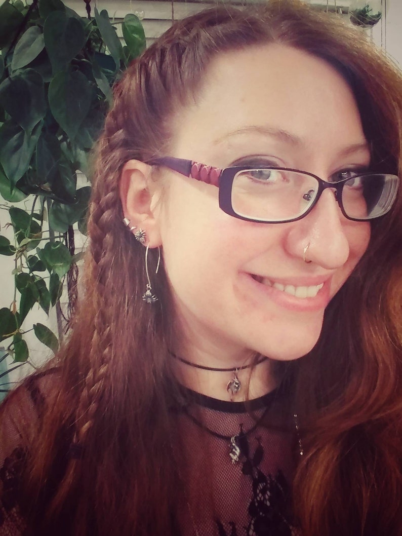 May include: A woman with long brown hair styled in a braid, wearing glasses, a black choker necklace, and a black lace top.