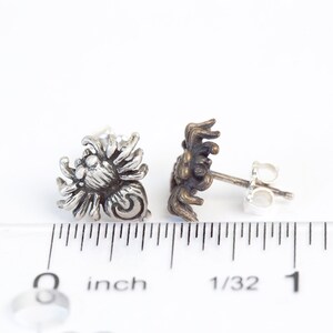 May include: A pair of silver spider earrings with a detailed design. The earrings are about 1/2 inch in size and have a post back.