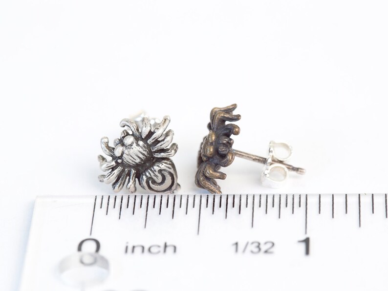 May include: A pair of silver spider earrings with a detailed design. The earrings are about 1/2 inch in size and have a post back.