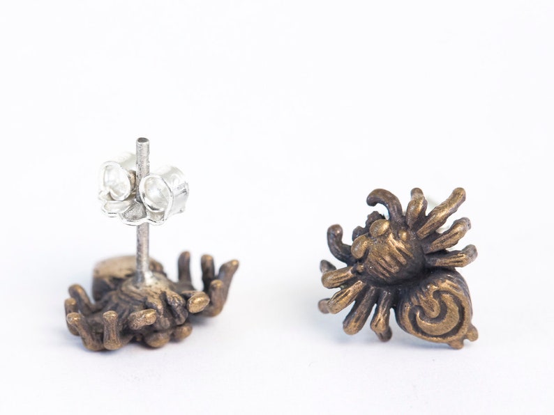 May include: A pair of bronze spider earrings with a detailed design. The earrings have a silver post and butterfly back.
