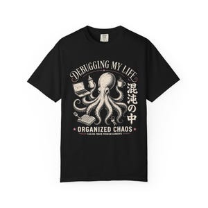 Peut inclure: Un t-shirt noir avec un motif représentant une pieuvre tenant un ordinateur portable, un biberon, une tasse de café, une spatule, un livre et des clés. Le texte indique "DEBUGGING MY LIFE", "ORGANIZED CHAOS", "EAGLION POWER PREMIUM GARMENTS" et des caractères japonais.