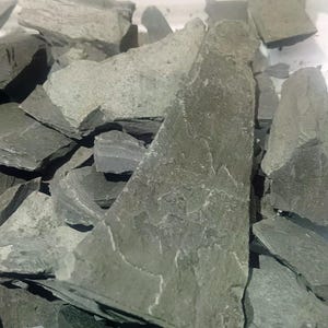 Peut inclure: Gros plan sur un tas de copeaux d'ardoise gris foncé. Les copeaux sont de forme irrégulière et ont une surface rugueuse et texturée.