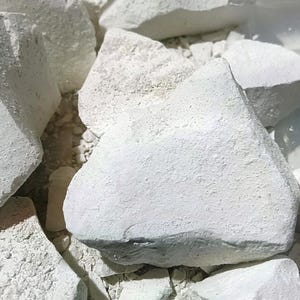 Op de afbeelding: Close-up van verschillende onregelmatig gevormde, gebroken witte krijtstukken. Het krijt heeft een ruw, getextureerd oppervlak en verschillende afmetingen. Sommige stukken zijn gebroken en onthullen een iets andere binnenkleur. De afbeelding is goed belicht.