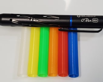 May include: A black Olight O-Pen Mini pen with a blue accent and a silver inscription. The pen is lying on top of six different colored pen refills: white, yellow, green, orange, red, and blue.
