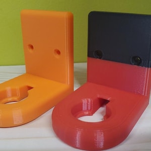 May include: Two 3D printed wall mounts, one orange and one with a black top and red bottom. Both mounts have a circular hole in the center and two small holes on the top.