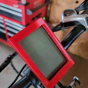 May include: A red 3D printed case with a screen inside, mounted on a black handlebar.