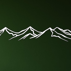 May include: A white outline of a mountain range on a dark green wall above a light wood cabinet with two drawers.
