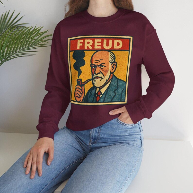 Może przedstawiać: Bordowa bluza z grafiką w stylu vintage przedstawiającą Zygmunta Freuda palącego fajkę, z napisem "FREUD" w czerwonym prostokącie. Ilustracja ma ż&oacute;łte tło i niebieski garnitur.