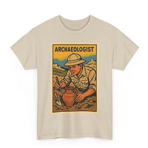 May include: Beige t-shirt featuring a vintage-style illustration of an archaeologist at work. The graphic shows a person in a khaki shirt and hat, excavating a clay pot. The word "ARCHAEOLOGIST" is printed at the top.