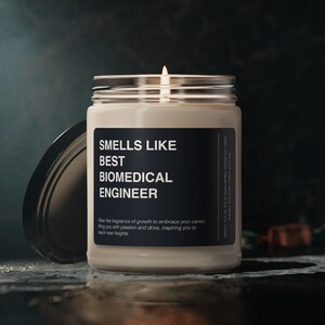 Pode incluir: Uma vela perfumada num frasco de vidro com uma etiqueta preta. A etiqueta diz "SMELLS LIKE BEST BIOMEDICAL ENGINEER". A tampa da vela está de lado. O texto abaixo diz "Permita que a fragrância do crescimento abrace sua carreira."