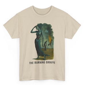 May include: Beige t-shirt featuring a surrealist painting. The artwork depicts a figure in a long blue dress, with a burning giraffe in the background. The text "THE BURNING GIRAFFE" is printed below the image.