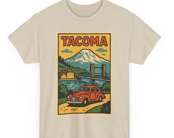 May include: Beige t-shirt with a vintage-style Tacoma, Washington graphic. The design shows a red car, a bridge, a mountain, and the word "TACOMA" in a yellow rectangle. The shirt is made of a soft, neutral-coloured fabric.