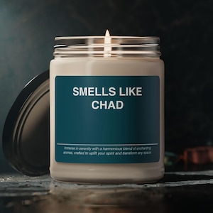 May include: A white candle in a glass jar with a teal label that reads "SMELLS LIKE CHAD". The label also includes the text "Immerse in serenity with a harmonious blend of enchanting aromas, crafted to uplift your spirit and transform any space."