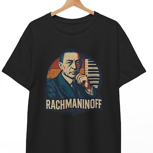 May include: A black t-shirt with a vintage-style illustration of Russian composer Sergei Rachmaninoff. The illustration features Rachmaninoff in a suit, with a keyboard in the background. The text "Rachmaninoff" is printed below the illustration.