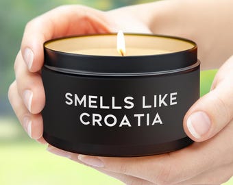 Może przedstawiać: Czarny słoik ze świecą z białą etykietą z napisem "Smells Like Croatia". Świeca jest zapalona, a słoik jest trzymany w dłoniach.