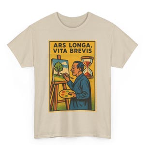 Peut inclure: T-shirt beige avec un motif rectangulaire portant l'inscription "ARS LONGA, VITA BREVIS". Le motif représente un artiste peignant un arbre sur une toile, avec un sablier. L'artiste porte un manteau bleu et tient une palette.
