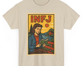 May include: Beige t-shirt featuring a retro-style graphic. The graphic depicts a woman reading a book, with the letters "INFJ" at the top. The illustration includes a landscape with a lake, trees, and a house, all in a vintage aesthetic.
