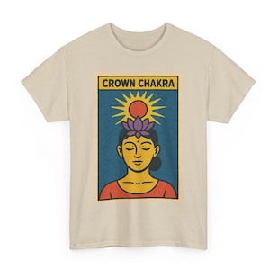 May include: Beige t-shirt featuring a graphic of a person meditating with a purple lotus flower on their head, a sun, and the words "CROWN CHAKRA" in a yellow rectangle. The design is on a blue background.