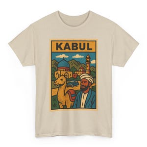 May include: Beige t-shirt featuring a colorful graphic of Kabul, Afghanistan. The design includes a camel, a man in traditional attire, and buildings. The word "KABUL" is displayed in bold letters at the top of the graphic.