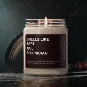 Puede incluir: Una vela blanca encendida en un tarro de cristal con tapa negra. La etiqueta dice "SMELLS LIKE BEST NAIL TECHNICIAN". El texto es visible debajo del texto principal.