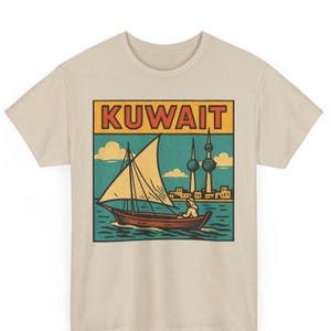 May include: Beige t-shirt with a retro graphic depicting a sailboat on the water, the word "KUWAIT" in a red and yellow box, the Kuwait Towers, and a blue and yellow sky. A vintage travel theme.