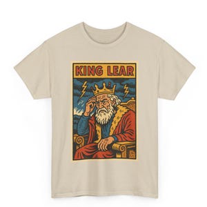 Puede incluir: Camiseta beige con un diseño de King Lear. La ilustración muestra una figura coronada y barbuda con una túnica roja, sentada en un trono, con el texto "KING LEAR" arriba. Rayos y un cielo tormentoso en el fondo.