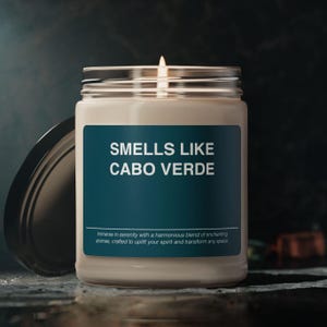 Peut inclure: Une bougie blanche dans un pot en verre transparent avec une étiquette bleu sarcelle qui indique "SMELLS LIKE CABO VERDE". L'étiquette comprend également le texte "Immerse in serenity with a harmonious blend of enchanting aromas, crafted to uplift your spirit and transform any space."