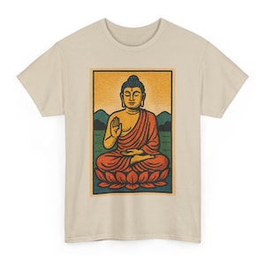 May include: Beige t-shirt featuring a vintage-style illustration of Buddha. The graphic depicts Buddha in a seated pose, wearing an orange robe, with a green and yellow background. The design is framed within a rectangular border.