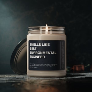 Pode incluir: Uma vela acesa num frasco de vidro com um rótulo preto que diz "Smells Like Best Environmental Engineer". A tampa do frasco está de lado. O texto abaixo diz "Allow the fragrance of growth to embrace your career, filling you with passion and drive, inspiring you to reach new heights."