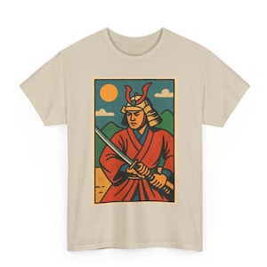 Pode incluir: Camiseta bege com um gráfico retangular de um guerreiro samurai. A ilustração mostra um samurai em vestes vermelhas e capacete, segurando uma espada. O fundo inclui um sol amarelo, céu azul e montanhas verdes.