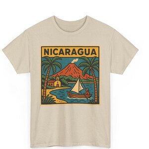 May include: Beige t-shirt with a rectangular graphic displaying "NICARAGUA". The image shows a volcano, palm trees, a boat, and a church. The design uses orange, blue, green, and brown colours.