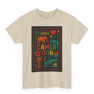 May include: A beige t-shirt featuring a colorful graphic design. The design includes the word "AFRICA" and "CAMEROON" with illustrations of an elephant, crocodile, hibiscus flower, and a heart.