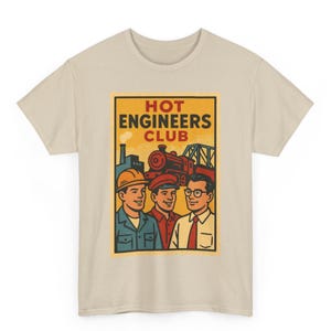 Pode incluir: T-shirt bege com um gráfico retangular com o texto "HOT ENGINEERS CLUB". O gráfico mostra três homens, um comboio e elementos industriais num estilo vintage. A t-shirt é feita de um tecido macio e de cor clara.