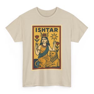 以下が含まれることがあります： ベージュ色のTシャツ。長方形のグラフィックには「ISHTAR」の文字。王冠をかぶり、花と星を持ち、ライオンがそばにいる女性が描かれています。デザインは黄色、オレンジ、青、赤の色を使用しています。