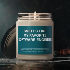 May include: A white candle in a glass jar with a teal label that reads "Smells Like My Favorite Software Engineer". The label also includes the text "Immerse in serenity with a harmonious blend of enchanting aromas, crafted to uplift your spirit and transform any space."