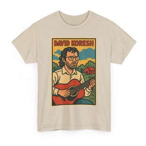 May include: A beige t-shirt featuring a graphic of a man playing a red guitar. The graphic includes the text "DAVID KORESH" in a rectangular frame, with a rural landscape background.