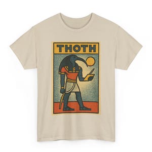 Puede incluir: Camiseta beige con un gráfico del dios egipcio Thoth. El diseño incluye la palabra "THOTH" en un rectángulo amarillo y azul, y una ilustración de Thoth sosteniendo una herramienta de escritura y un sol. La obra de arte está en tonos de azul, rojo, naranja y beige.