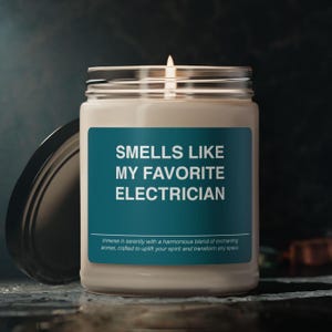 May include: A lit candle in a glass jar with a silver lid. The label reads "SMELLS LIKE MY FAVORITE ELECTRICIAN." Below the text is a description of the candle's aromas. The jar is open, revealing the candle inside.