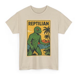 May include: Beige t-shirt featuring a retro-style graphic of a green reptilian humanoid with red eyes, standing on a beach with palm trees and the word "REPTILIAN" in a black rectangle.