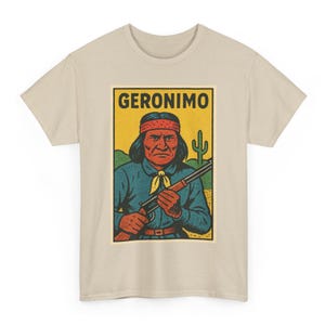 May include: Beige t-shirt featuring a vintage-style graphic of Geronimo. The illustration shows Geronimo in a blue shirt, red headband, and holding a rifle, with the word "GERONIMO" above him. A cactus and desert landscape are in the background.