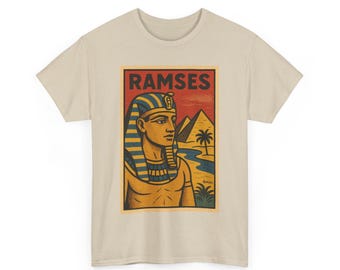 Puede incluir: Camiseta beige con un gráfico de Ramsés, un antiguo faraón egipcio. El gráfico incluye la palabra "RAMSES" en rojo, un perfil de Ramsés, pirámides y palmeras. El diseño es de estilo vintage.