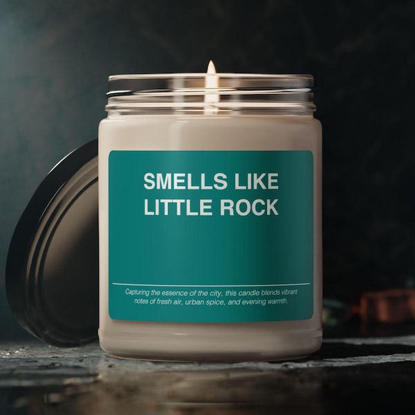 May include: A glass candle jar with a teal label that reads "Smells Like Little Rock". The label also includes the text "Capturing the essence of the city, this candle blends vibrant notes of fresh air, urban spice, and evening warmth."
