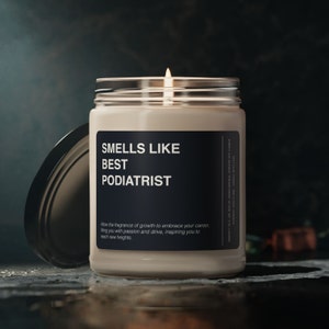 May include: A lit candle in a glass jar with a silver lid. The label reads "SMELLS LIKE BEST PODIATRIST." The text below says "Allow the fragrance of growth to embrace your career, filling you with passion and drive, inspiring you to reach new heights."