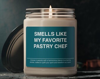 May include: A lit candle in a glass jar with a silver lid. The label reads "SMELLS LIKE MY FAVORITE PASTRY CHEF". The candle is white, and the label is teal. The text at the bottom of the label reads "Immerse in serenity..."