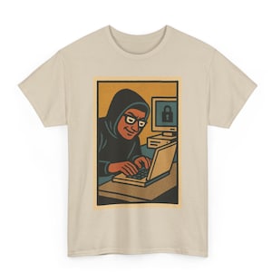 Puede incluir: Camiseta beige con una ilustración retro de una persona con capucha y gafas, escribiendo en un portátil. Un monitor de ordenador con un icono de candado es visible. El diseño tiene una estética vintage de cómic.